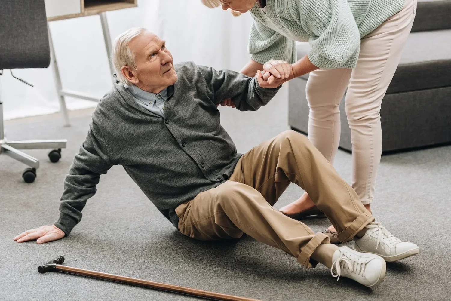 A senior man being helped up after a fall in his living room